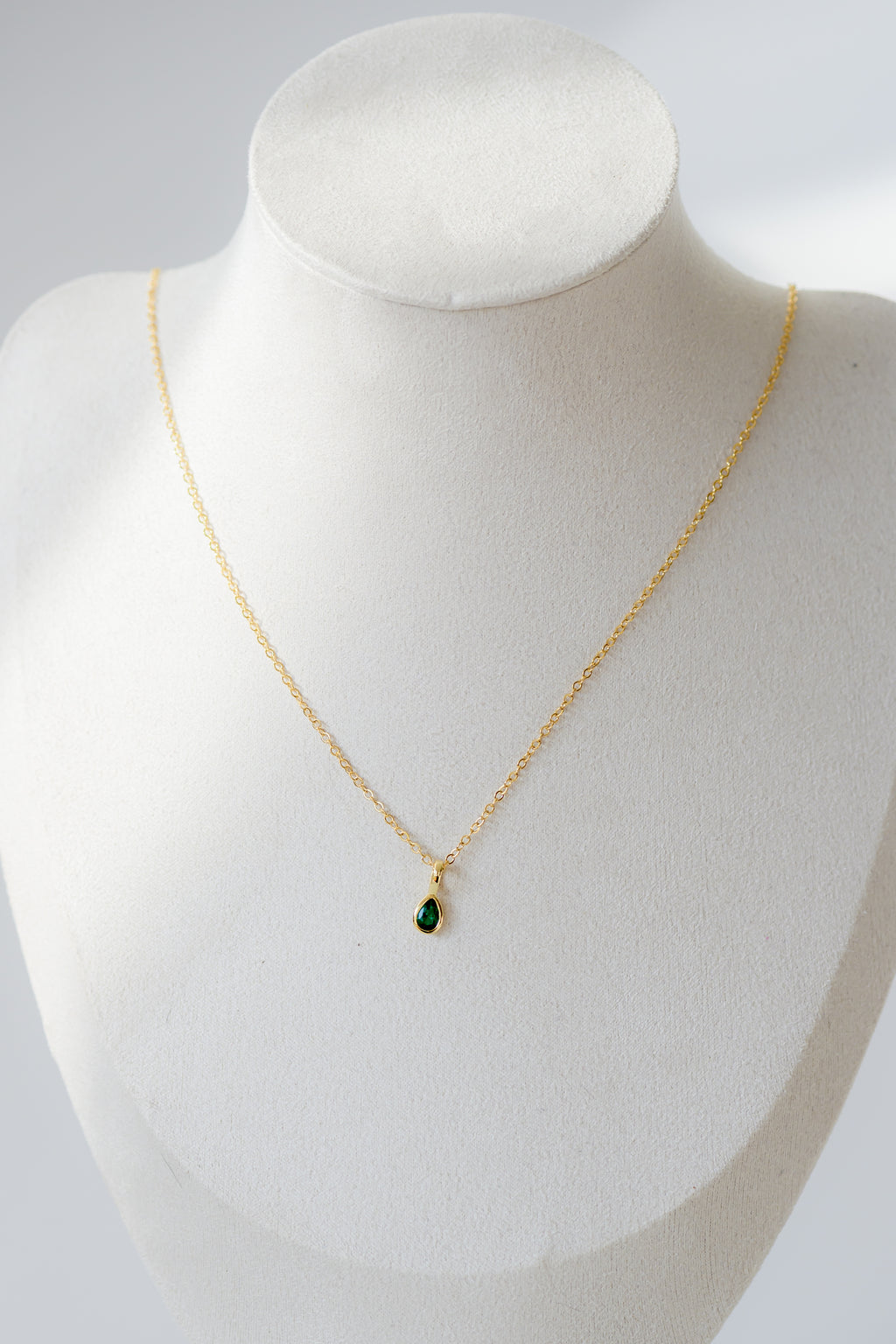 Gold necklace with a green pendant on a mannequin bust against a white background