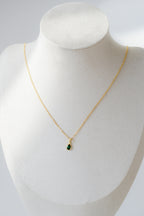 Gold necklace with a green pendant on a mannequin bust against a white background
